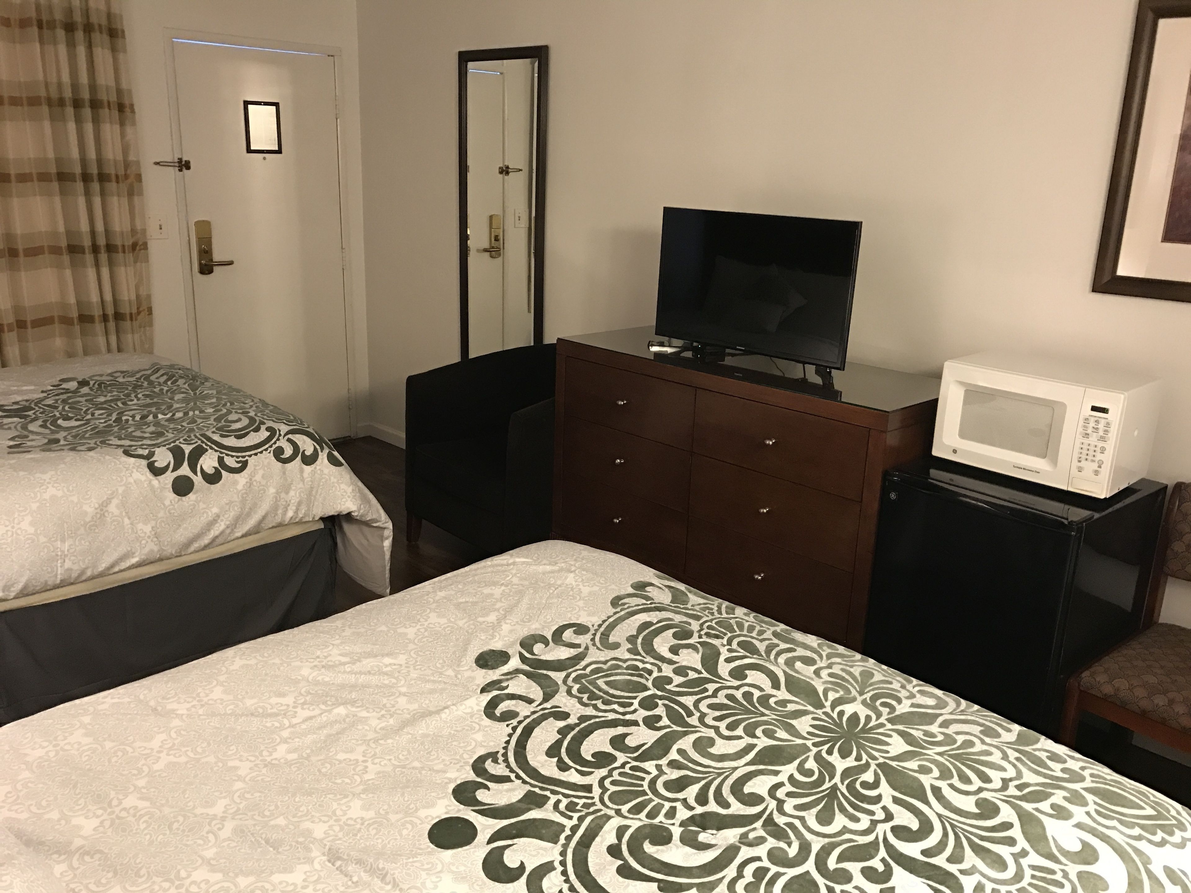 A hotel room with two beds, a TV on a dresser, a microwave, and a door with a mirror.