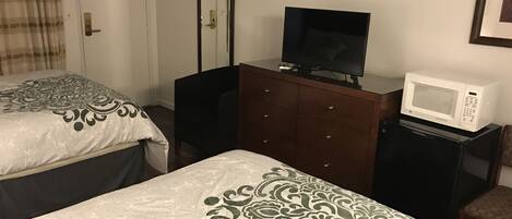 Habitación de hotel con dos camas, un televisor en una cómoda, un microondas y una puerta con espejo.