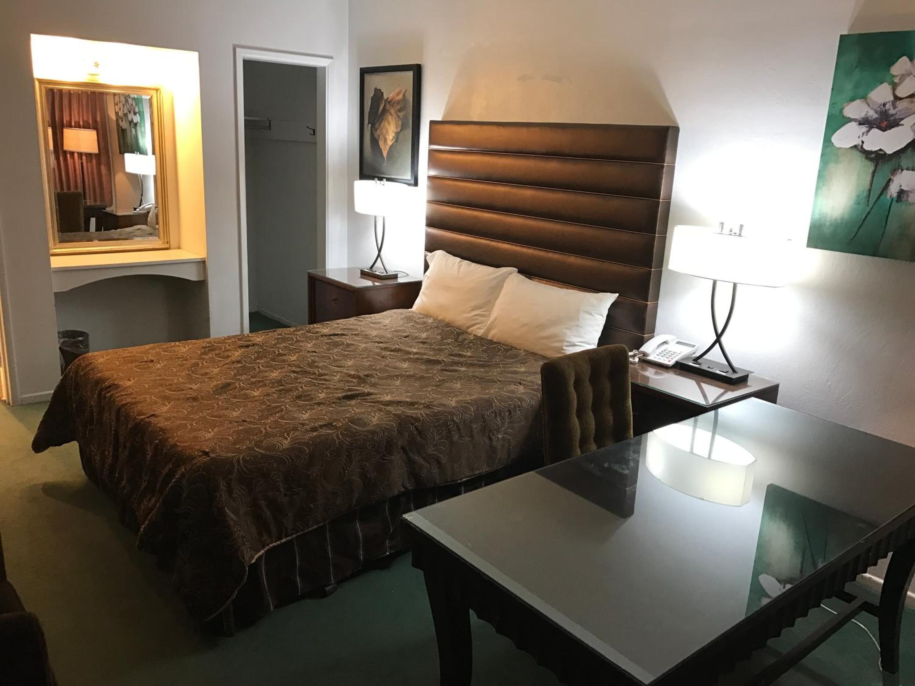 Une chambre d’hôtel avec un grand lit, un bureau, une chaise, une table de chevet, une lampe et un tableau au mur.