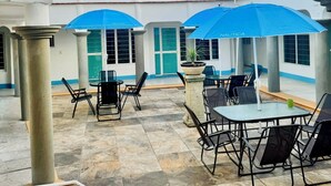A courtyard with outdoor seating, covered by blue umbrellas, and a building with a tiled roof and balconies. - Casa Porfirio (Oaxaca)
