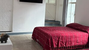 A bedroom with two beds, a flat-screen TV, an air conditioning unit, and a staircase leading to an upper floor. - Casa Porfirio (Oaxaca)