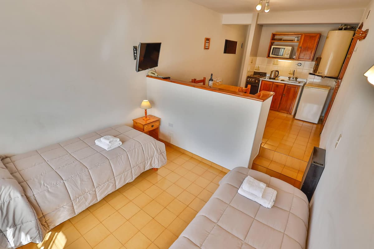 Una habitación con dos camas, una pequeña cocina y un televisor en la pared.