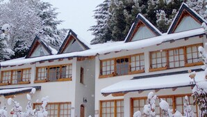 A multi-story building with a traditional architectural style, featuring wooden window frames and a snow-covered roof. - La Ponderosa Apart Hotel (San Carlos de Bariloche)