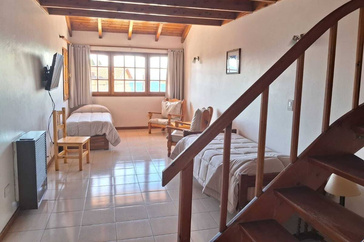 Un dormitorio con escaleras de madera, una cama, una silla, un escritorio y una ventana con cortinas.