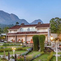 Una casa de dos pisos con jardín delantero, una montaña al fondo y cielo despejado.