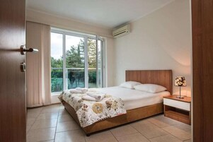 Un dormitorio con una cama grande, una mesita de noche, una ventana con cortinas y un equipo de aire acondicionado.