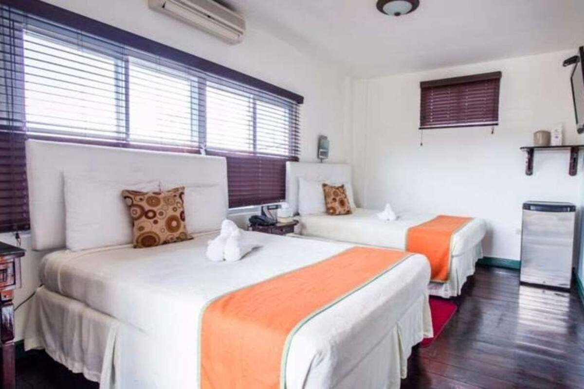 Une chambre d’hôtel avec deux lits, une petite table, une chaise, un téléviseur et une fenêtre avec des stores.
