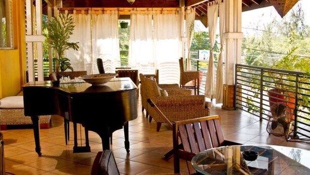 Un espace extérieur abrité, aménagé avec un piano, des fauteuils en osier et une table en verre.