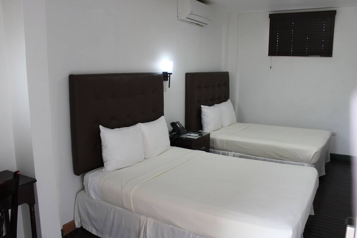 Une chambre d’hôtel avec deux lits, une table de chevet avec un téléphone et un climatiseur fixé au mur.