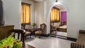 Habitación de hotel con una cama, zona de estar con una mesa y sillas, y vista a otra habitación por un arco.