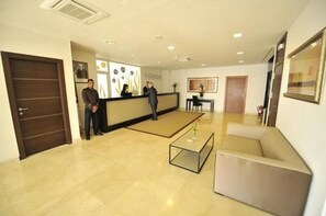 Rebedor d'hotel amb taulell de recepció, un sofà, una taula de cafè i una porta.