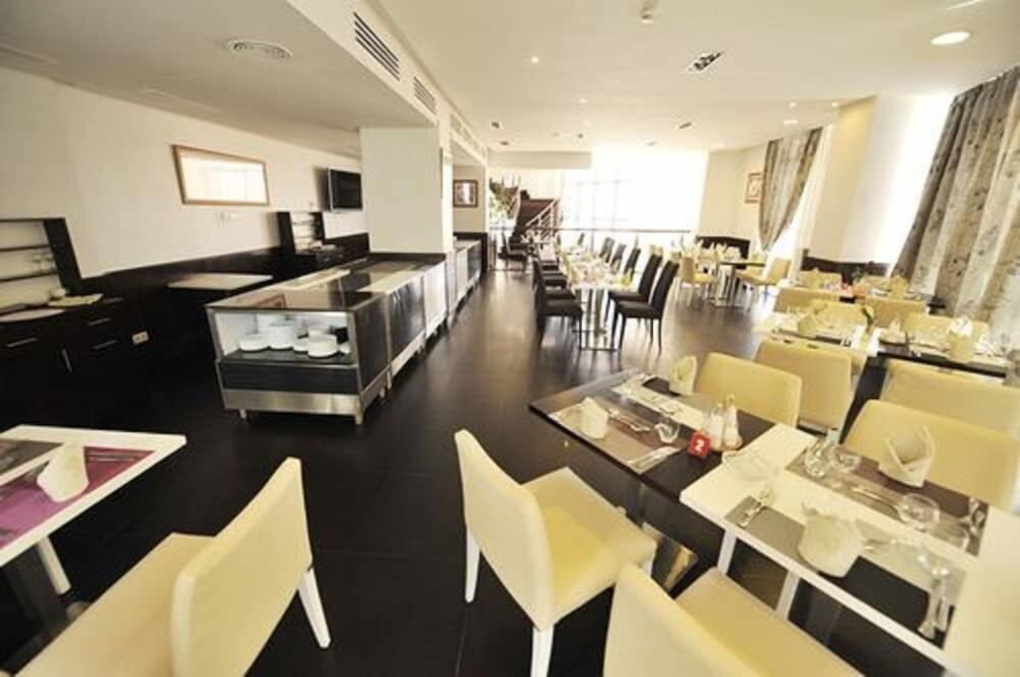 Un hall d’hôtel comprenant un comptoir d’accueil, un espace repas avec des tables et des chaises, et un escalier menant à un autre étage.