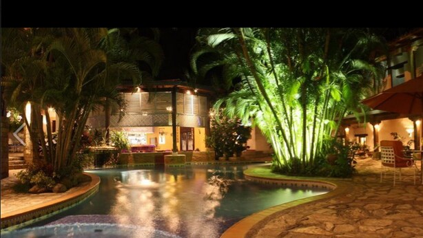 A nighttime pool area with a water feature, palm trees, and outdoor seating. - Marina (Copan)