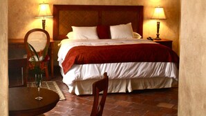 A bedroom with a wooden ceiling, a bed with white and red bedding, two bedside lamps, a wooden chair, and a small table with a vase. - Marina (Copan)