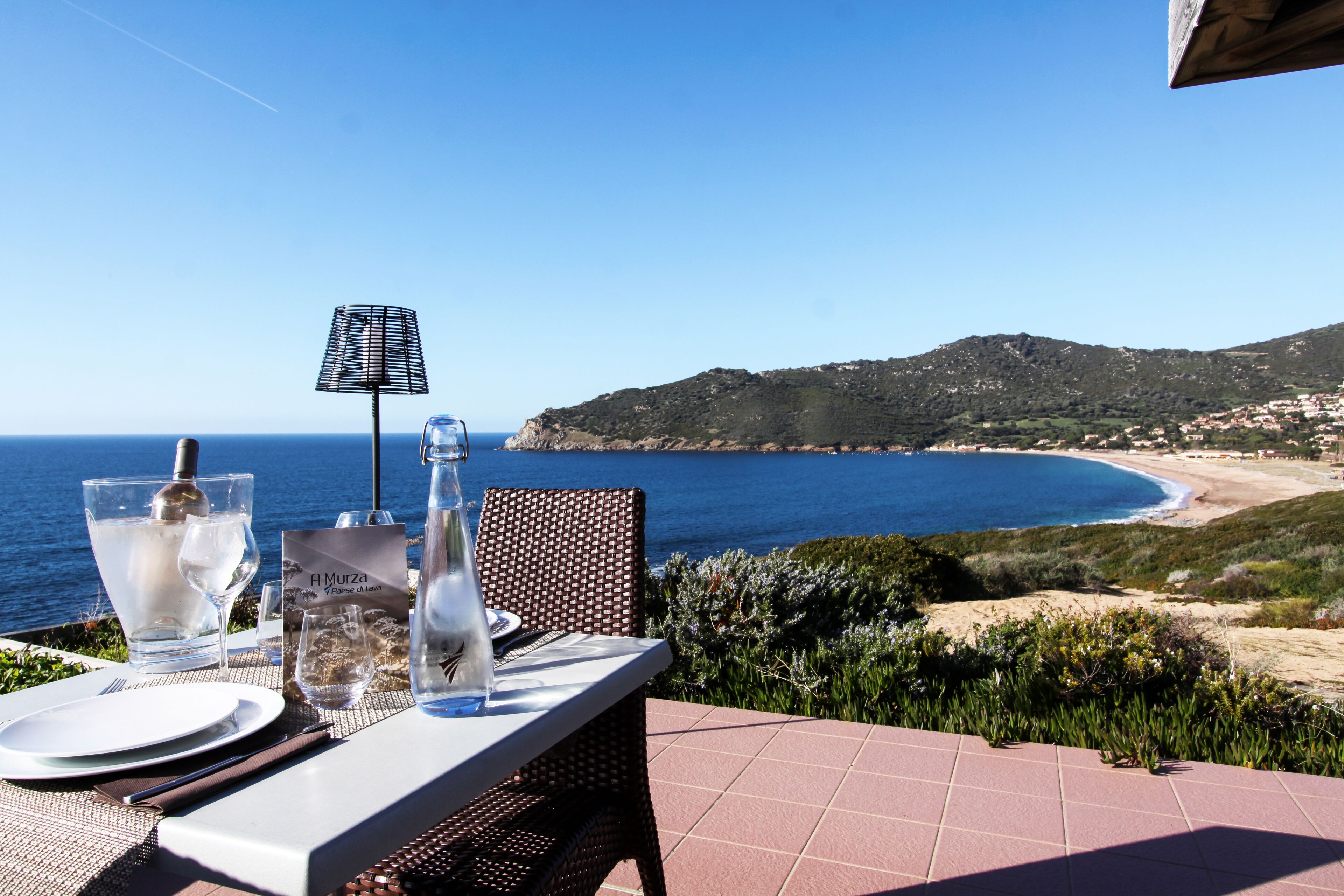 A table set for two with a view of the sea and a mountainous landscape.