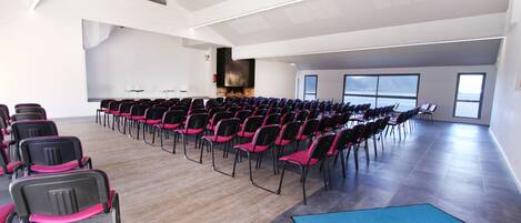 A conference room with rows of chairs, a stage, and a fireplace.