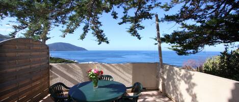 A patio with a table and chairs, overlooking a beach and the sea.