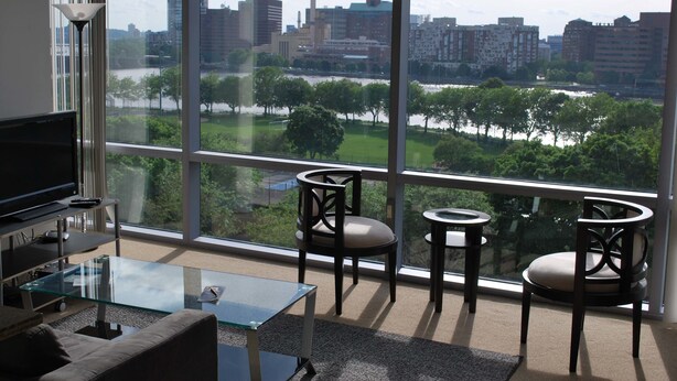 Una sala de estar moderna con un ventanal grande, un televisor de pantalla plana, una mesa de centro de vidrio y dos sillones.