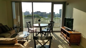 Una sala de estar con sofá, mesa de centro, televisor sobre un mueble de madera y balcón con vista a la ciudad.