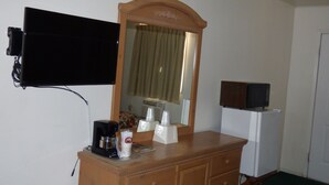 A hotel room with a wooden dresser, a flat-screen TV mounted on the wall, a mirror above the dresser, and a refrigerator in the corner. - Carrizozo Inn (Carrizozo)