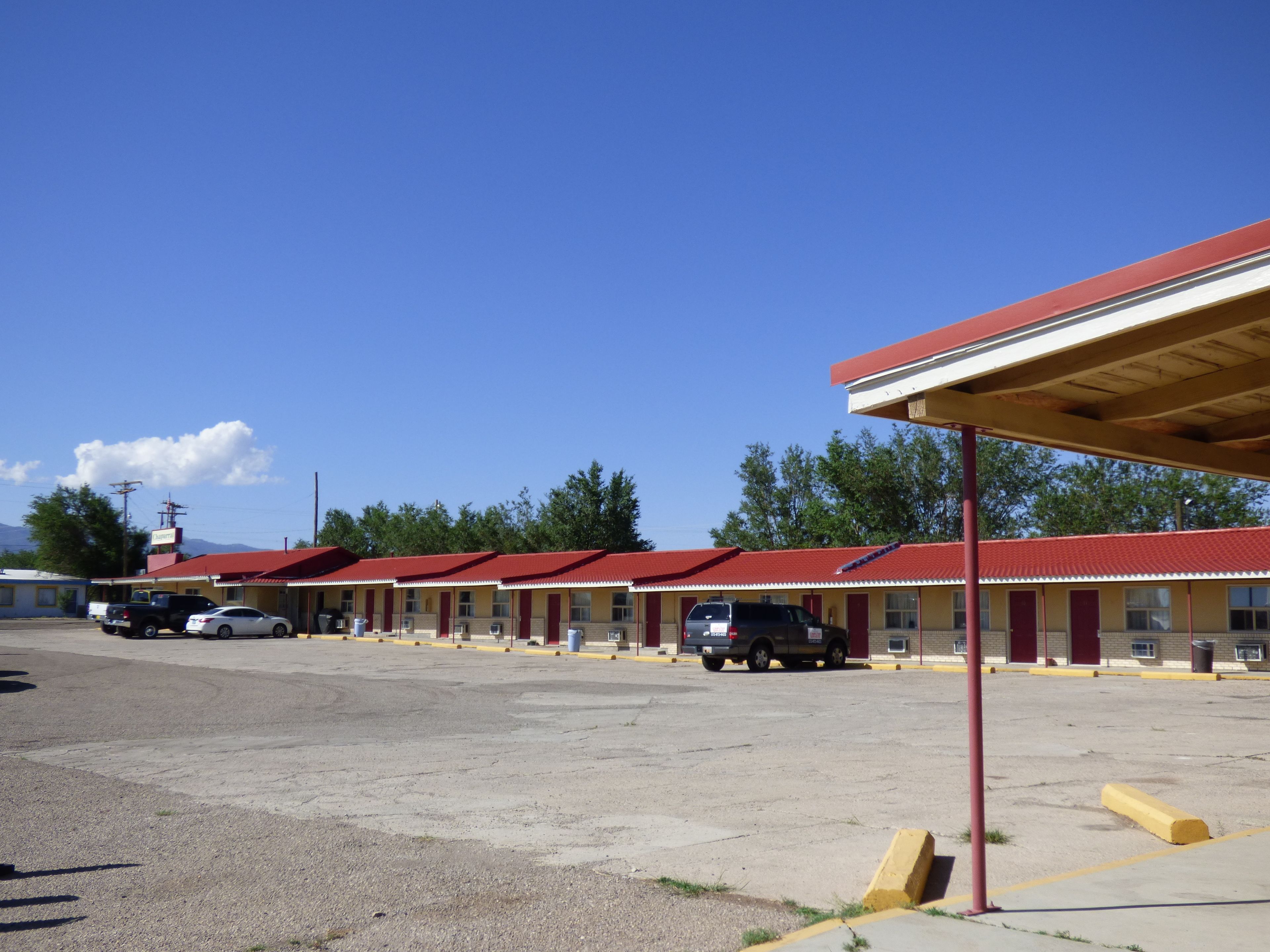 A motel with multiple rooms, a covered parking area, and a clear sky.