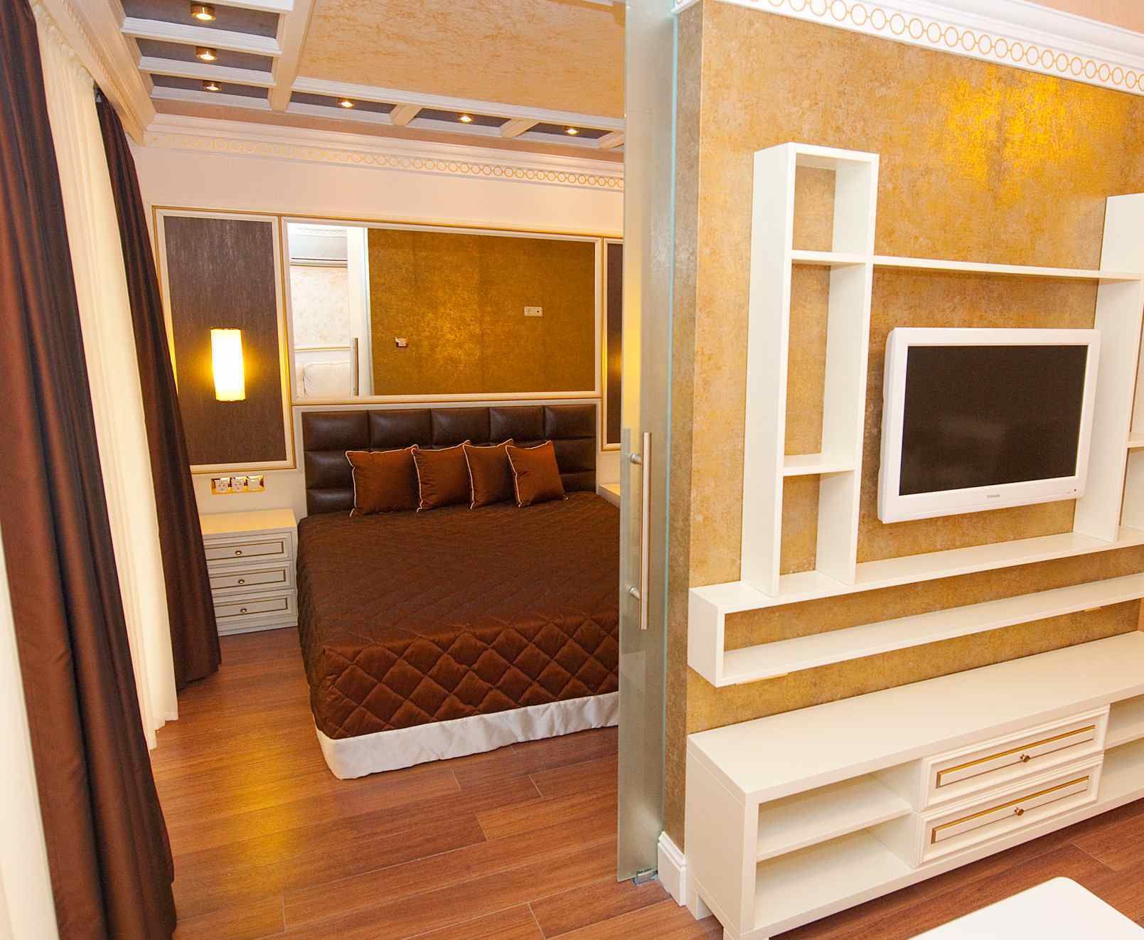 A hotel room with a large bed, a TV mounted on the wall, and a bedside table.
