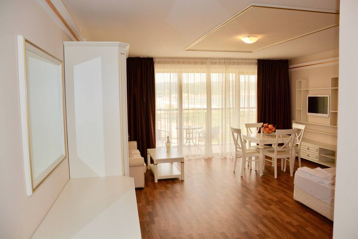 A modern, well-lit room with a dining area, a sofa, and a TV.