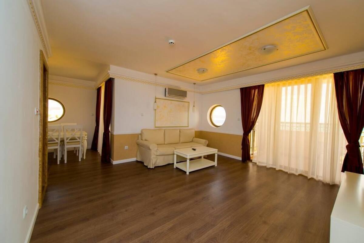A spacious living room with a wooden floor, a beige sofa, a small coffee table, and a dining area with a table and chairs.