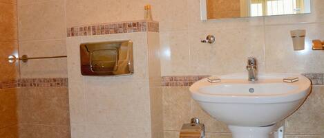 A bathroom with a toilet, sink, mirror, and shower.