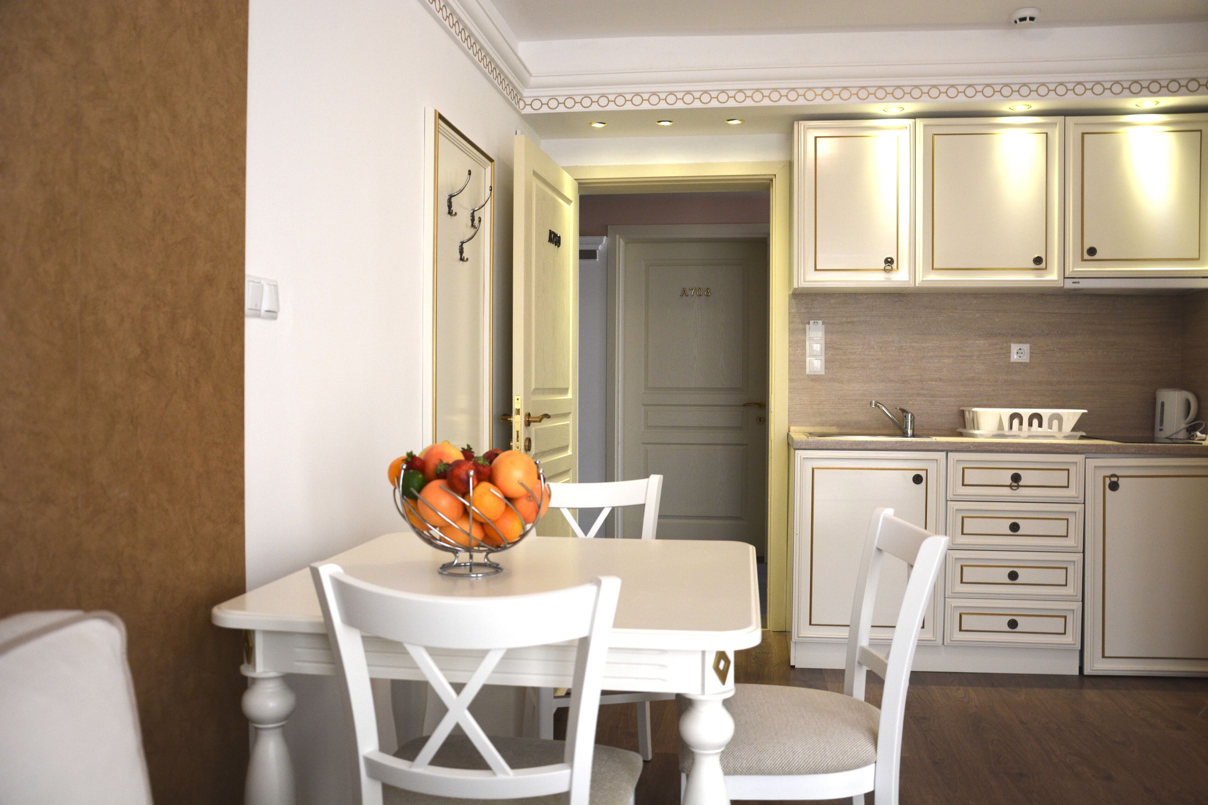 A dining area with a table and chairs, a bowl of fruit, and a kitchen with cabinets and a sink.