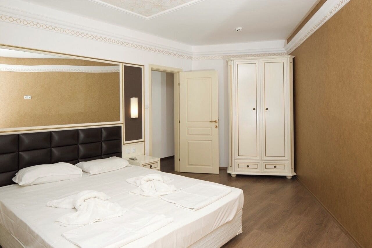 A hotel room with a large bed, a wardrobe, and a mirror.