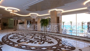 A spacious lobby with a decorative floor pattern, a balcony with a railing, and a view of a pool. - Golden Rainbow VIP Residence (Sunny Beach)