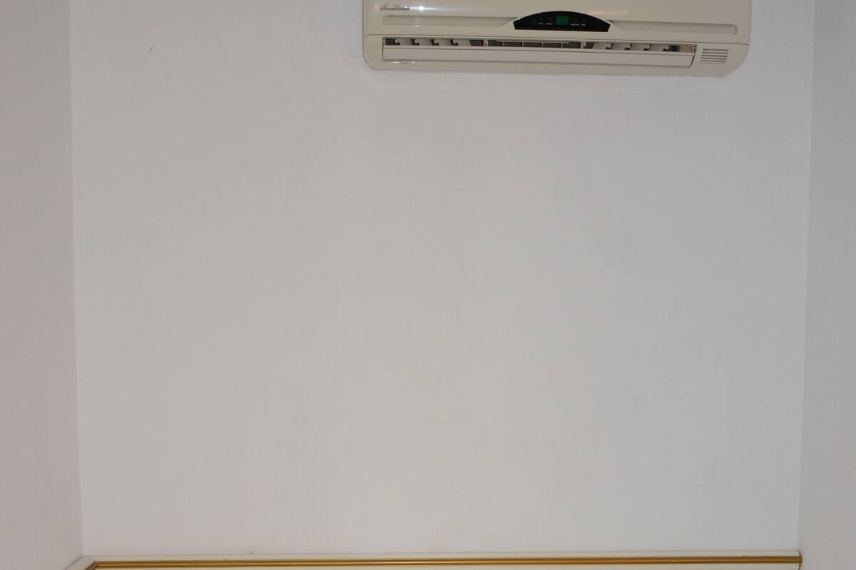 A hotel room with a single bed, a white pillow, a folded towel, and an air conditioning unit on the wall.