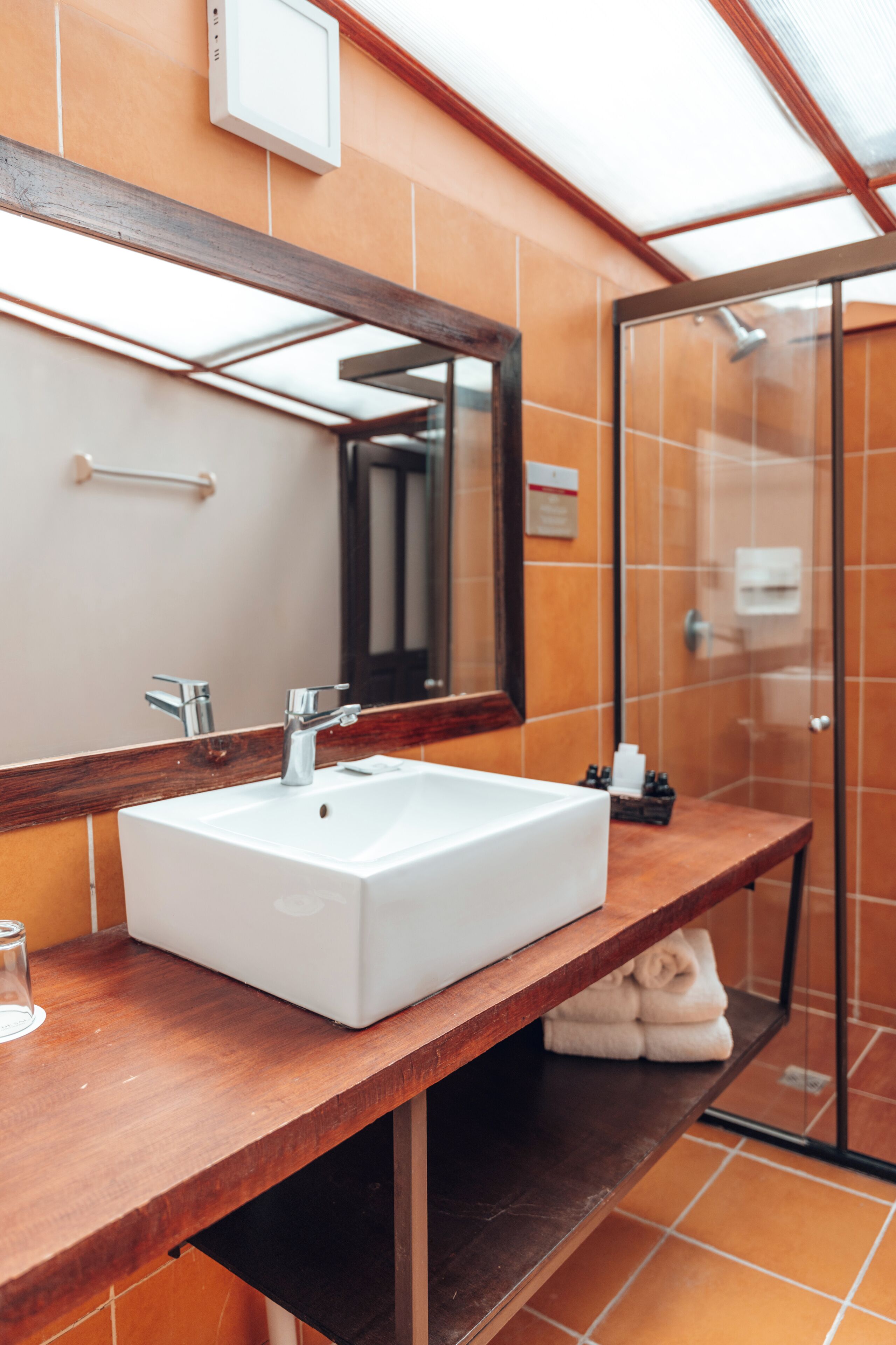 A bathroom with a white sink, a wooden countertop, a mirror, and a glass shower enclosure.
