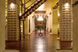 Um hall amplo com piso de madeira, uma escadaria e um lustre central.