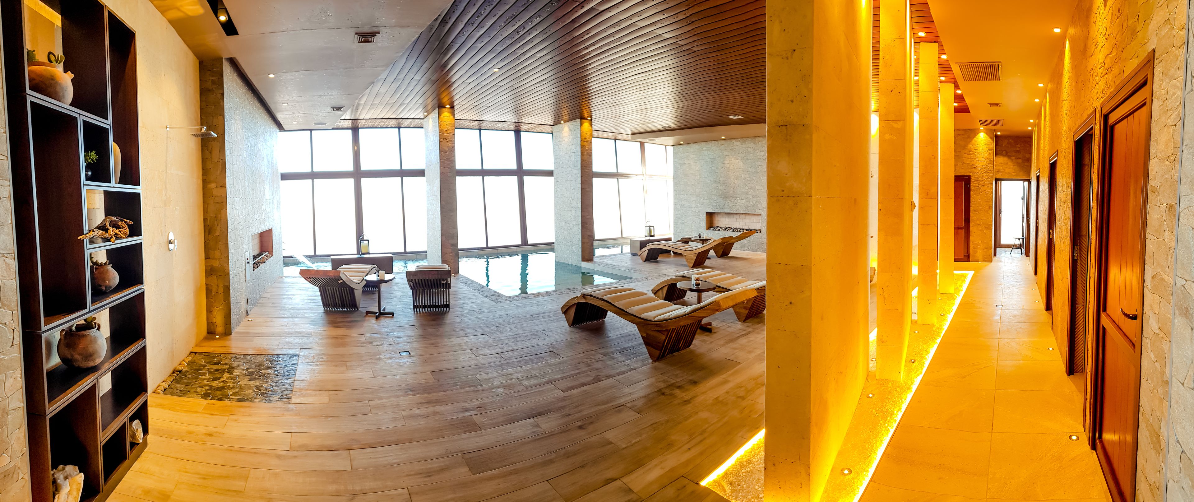 Un espacio interior amplio con suelo de madera, una piscina y una zona de estar con tumbonas.