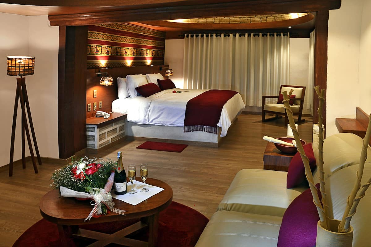 A hotel room with a bed, bedside table, lamp, chair, and a small table with a bouquet and drinks.