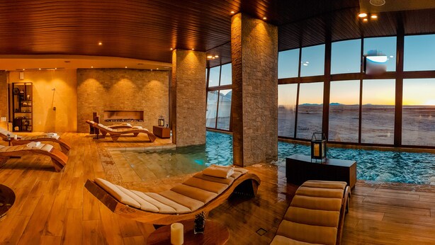 A spa with wooden floors, lounge chairs, a stone wall, and a large window overlooking a desert landscape. - Hotel Palacio de Sal (Uyuni)