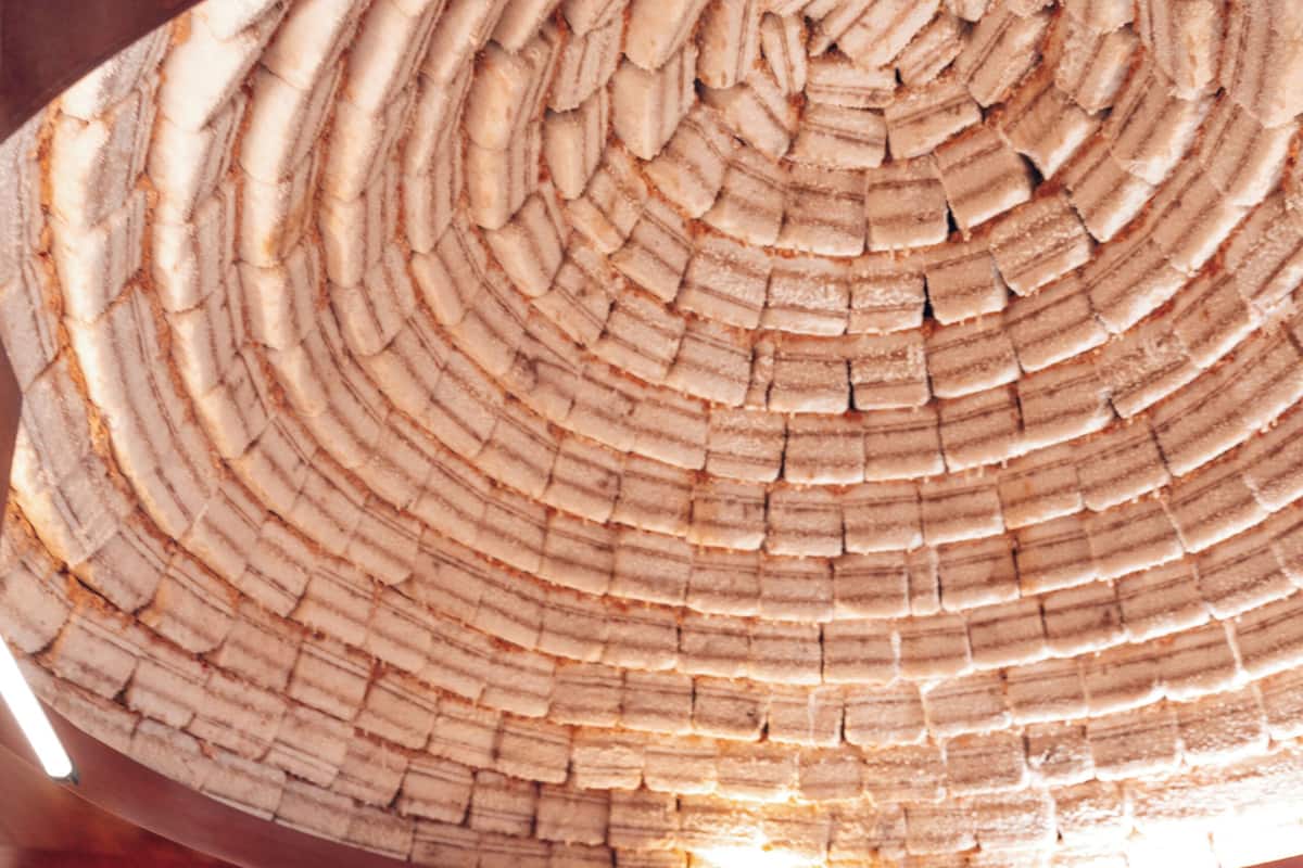 A bed with a red and white bedspread, a wooden headboard with a patterned design, and a circular ceiling made of stacked materials.