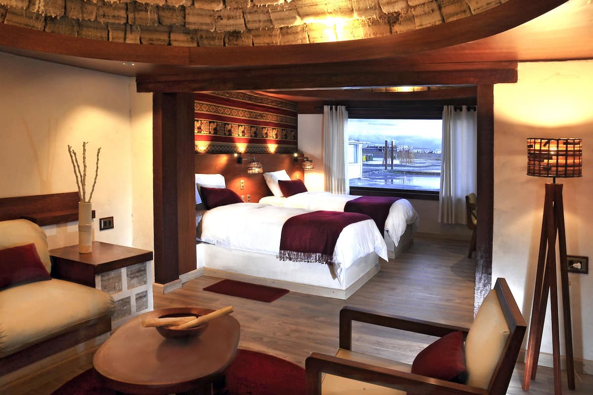 A hotel room with a large bed, a sofa, a small table, and a view of the beach through the window.