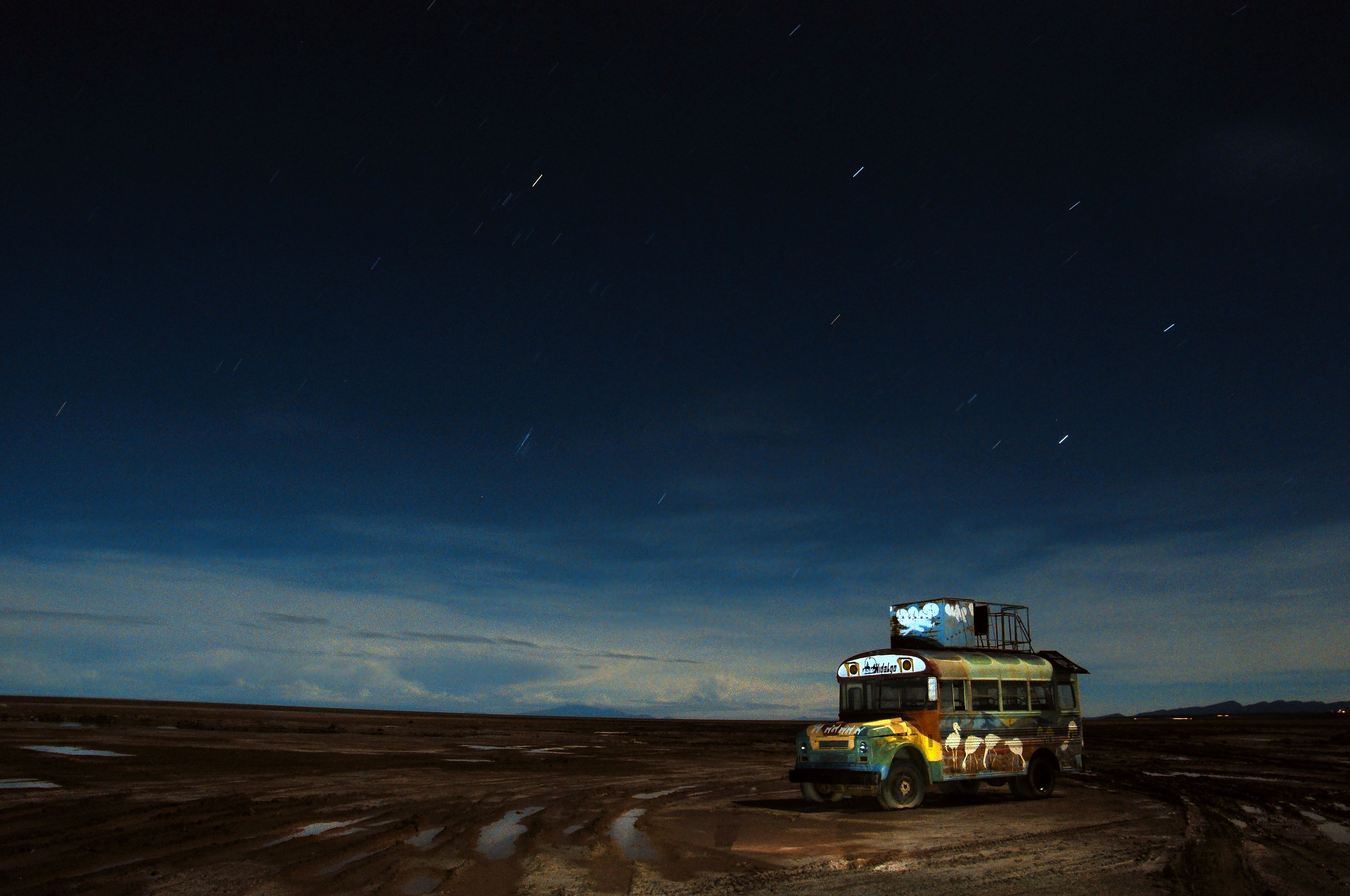 Un autobús estacionado en un camino de tierra bajo un cielo estrellado.