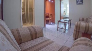 Un salon avec des canapés à motifs, une table basse en verre et une porte donnant sur une salle de bain.