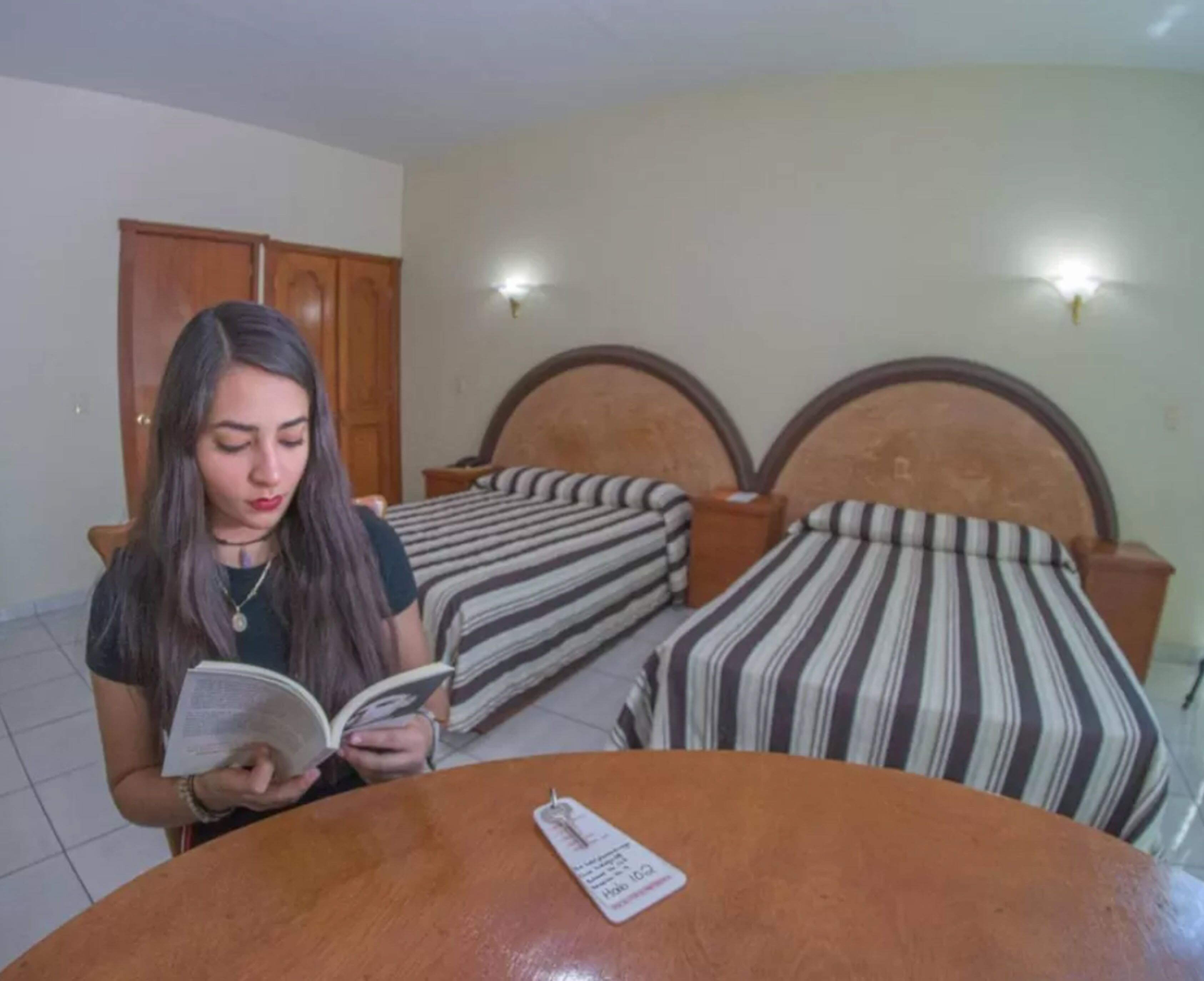 A room with two beds, a wooden table, and a wall-mounted light fixture.