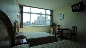 Une chambre d’hôtel avec deux lits, une fenêtre donnant sur un bâtiment historique, une table avec des chaises et un téléviseur fixé au mur.