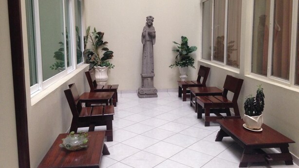 Un couloir étroit orné d’une statue, de plantes en pot et de tables et chaises en bois.