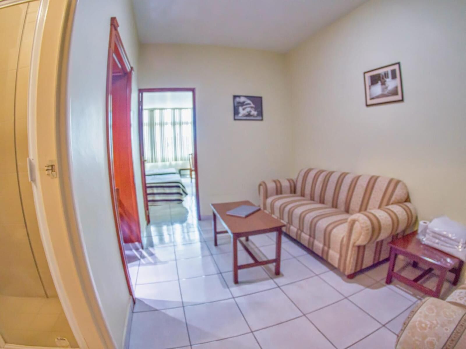 Una sala de estar con un sofá a rayas, una mesita y una silla. Hay una puerta que da a un balcón con vistas al exterior.