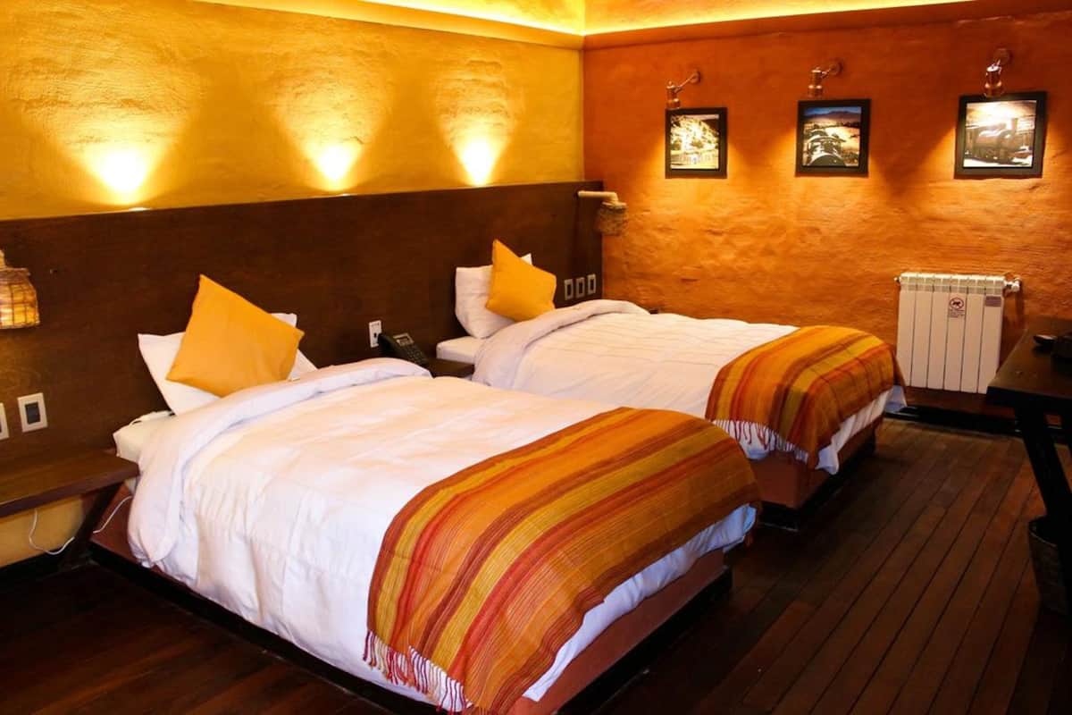 Een hotelkamer met twee bedden, houten vloeren en wandlampen.