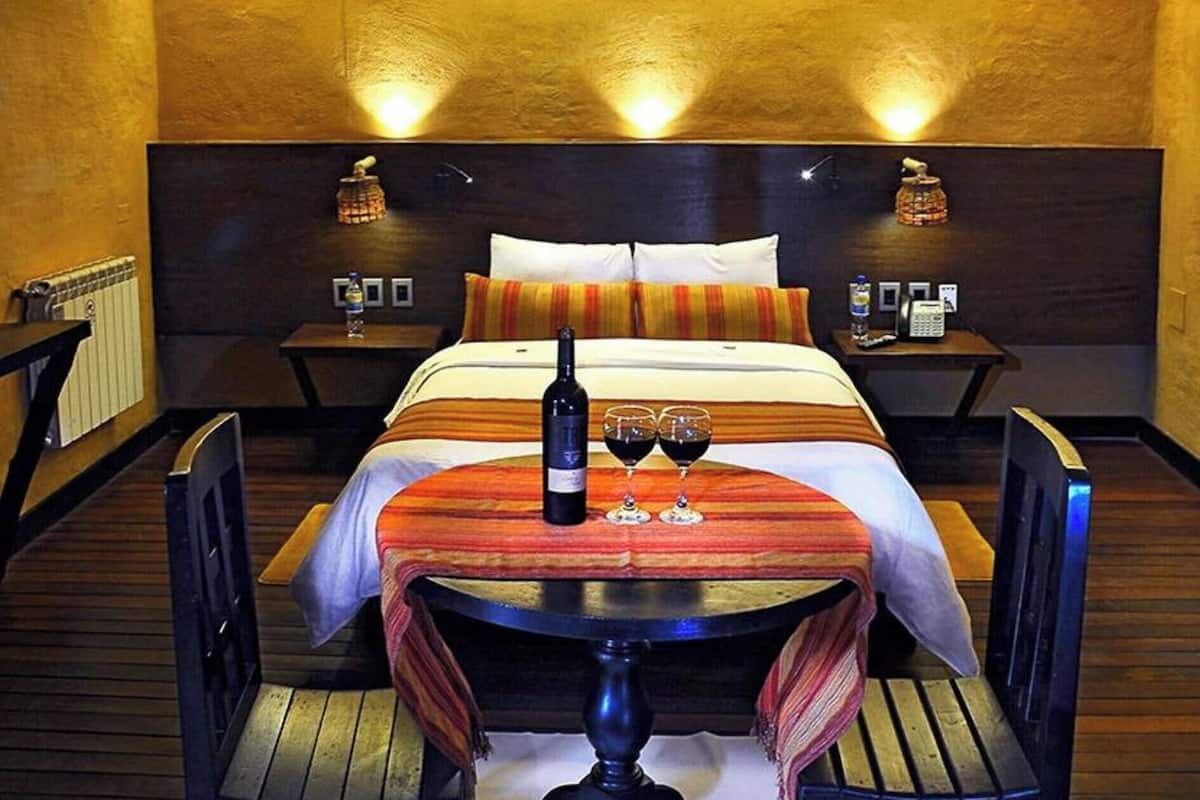 Een hotelkamer met een bed, nachtkastjes, een tafel met wijnglazen, een fles en een stoel.