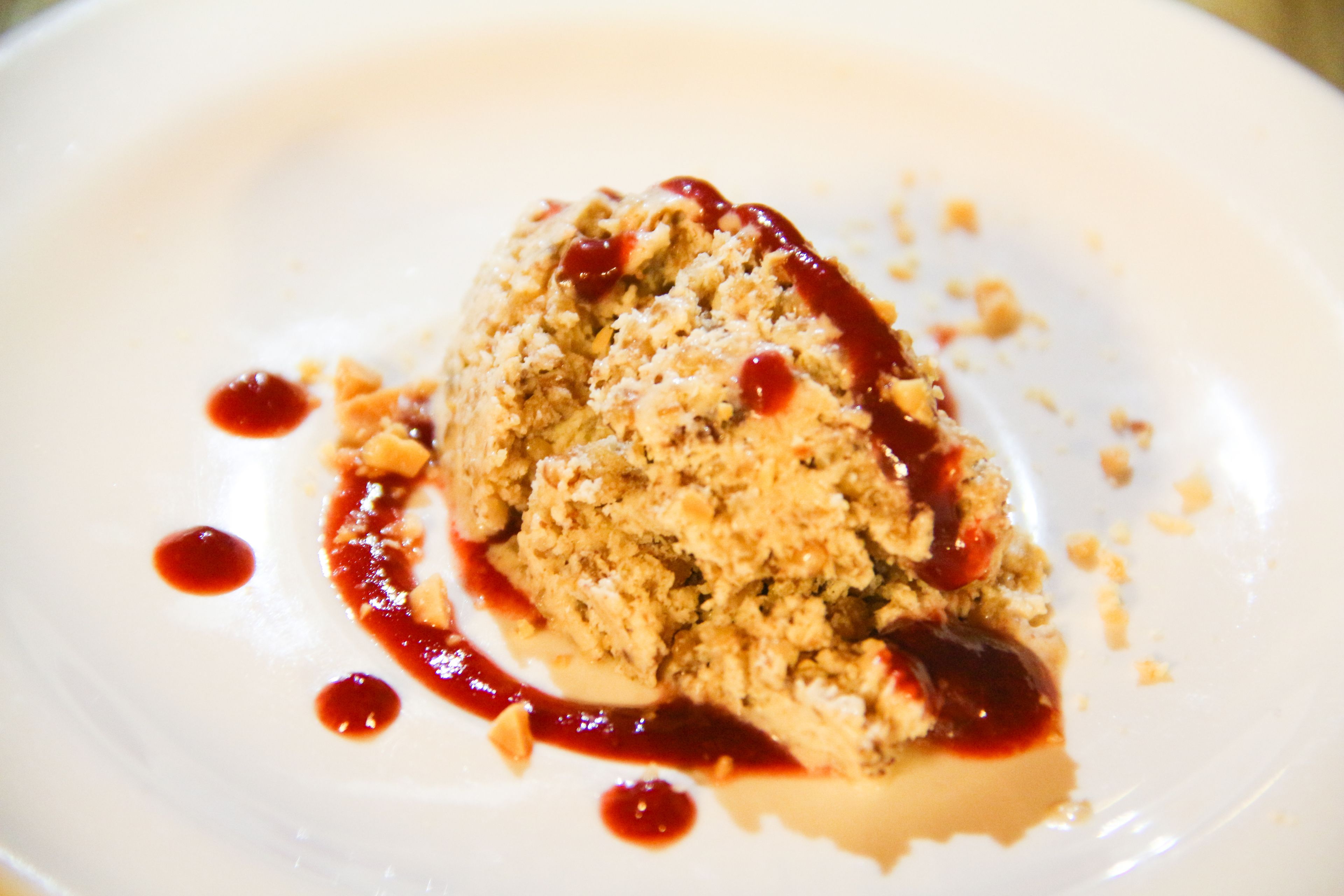 A dessert on a white plate with a crumbly topping and red sauce.