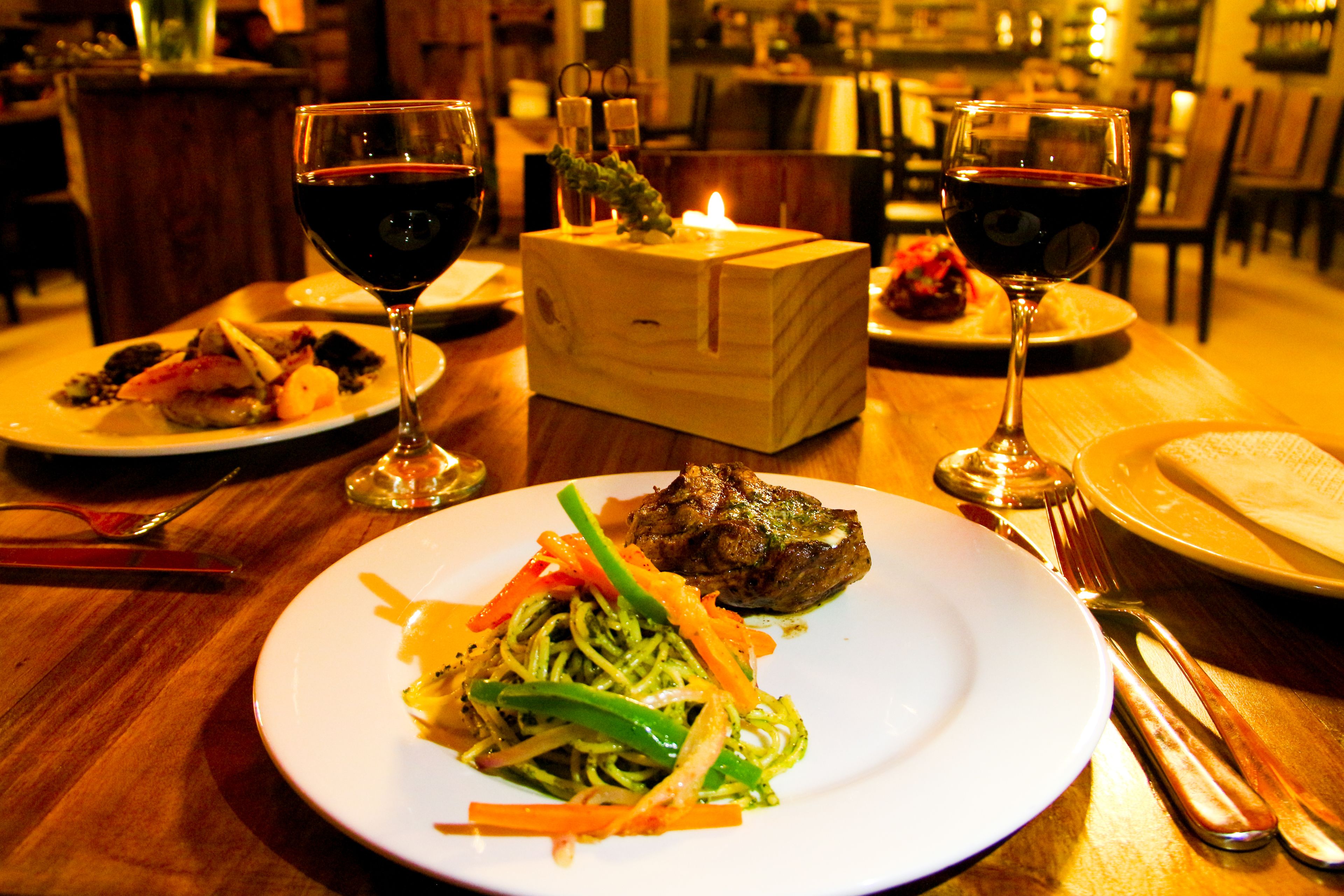 A dining table with plates of food, wine glasses, and a lit candle.